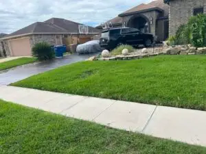Mowed front yard featuring a landscaped bed with decorative boulders, stone border, and mature landscaping