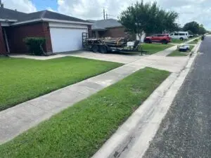 Freshly mowed front lawn with crisp edging in front of a brick single-story home, service trailer parked in driveway.
